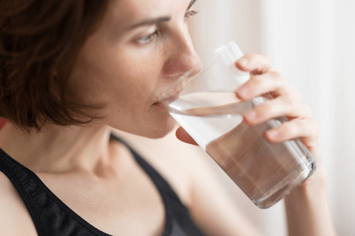 A woman in athletic wear drinks a glass of water,