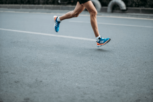 Close-up of a runner’s legs in motion on an empty road, wearing blue Adidas running shoes
