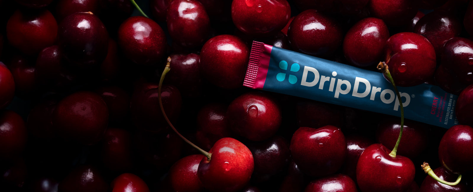 DripDrop electrolyte powder surrounded by cherries on a dark background