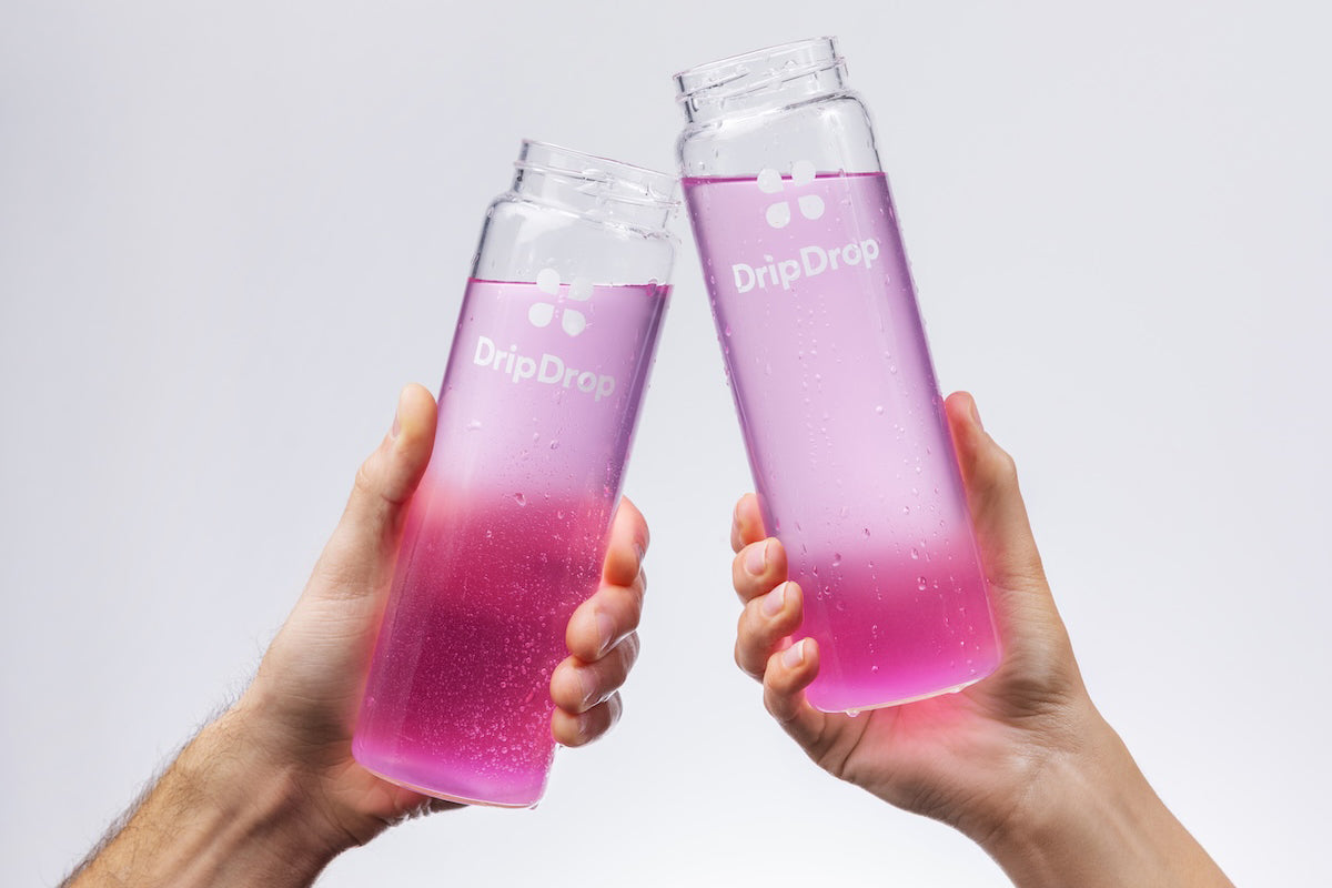 Two hands holding DripDrop bottles with pink liquid against a light gray background