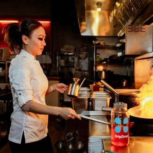 Woman in a professional kitchen cooking with a bottle of DripDrop on the counter next to her