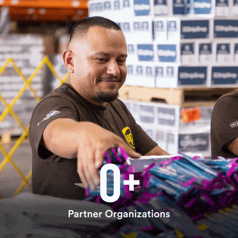 A man in a UPS uniform packing sticks of DripDrop in boxes with a pile of DripDrop boxes in the background with 33+ Partner organizations in text overlay