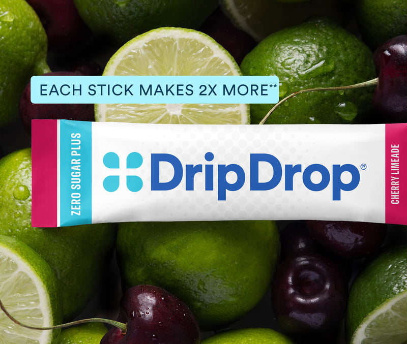 A DripDrop Zero Sugar Plus Cherry Limeade stick pack placed over a close-up background of limes and cherries. The package is white with blue branding and pink side accents, with a light blue text banner above reading 'EACH STICK MAKES 2X MORE'.