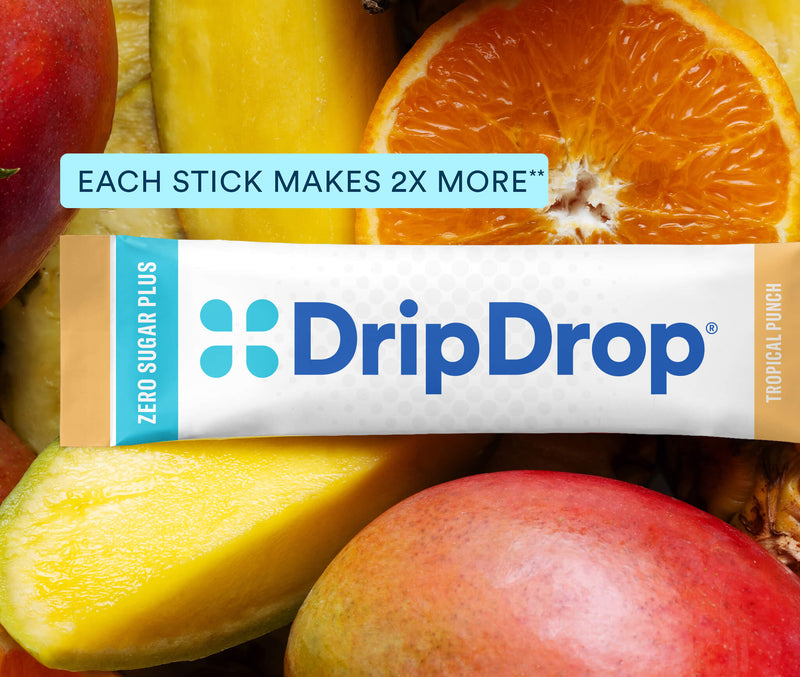 A DripDrop Zero Sugar Plus Tropical Punch flavored stick is centered over a close-up background of sliced mangoes and orange fruit. Text on the image reads 'EACH STICK MAKES 2X MORE' and 'DripDrop' branding is clearly visible on the stick packaging.