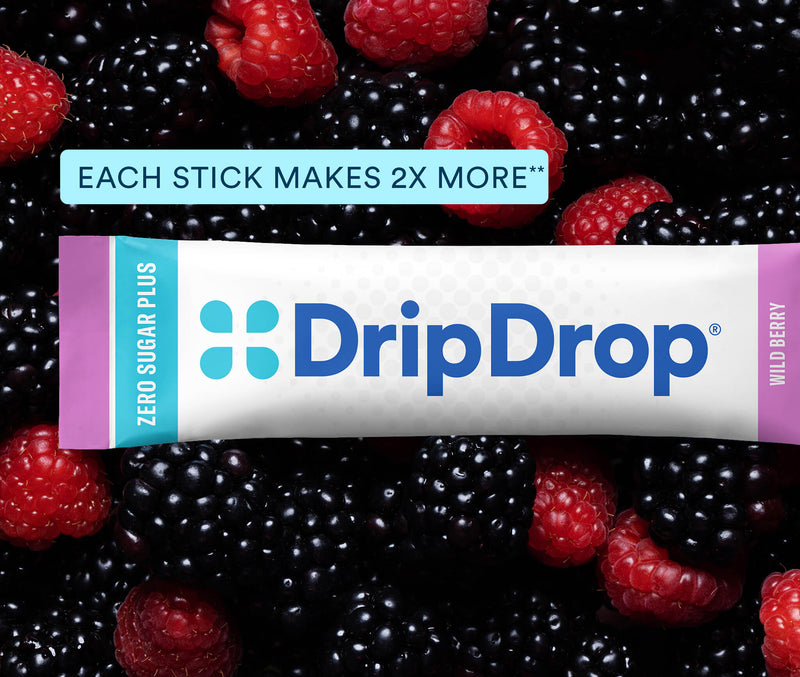 A DripDrop Zero Sugar Plus wild berry stick product shown wrapped in its white, blue, and pink packaging, placed over a close-up background of fresh blackberries and raspberries. A text banner at the top reads 'EACH STICK MAKES 2X MORE'.