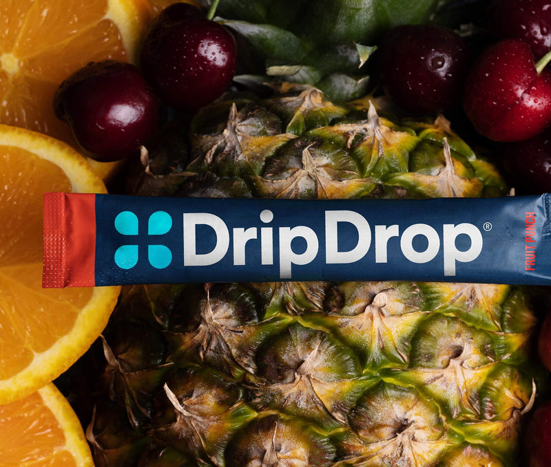 A DripDrop stick package laid across a close-up arrangement of fresh fruit, including pineapple, cherries, and orange slices.