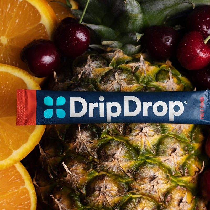 A DripDrop stick package laid across a close-up arrangement of fresh fruit, including pineapple, cherries, and orange slices.