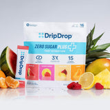 A bag and tube of DripDrop Zero Sugar Plus fast hydration drink mix are centered on a white reflective surface, surrounded by fruit slices and whole fruits including pineapple, watermelon, orange, and raspberries.