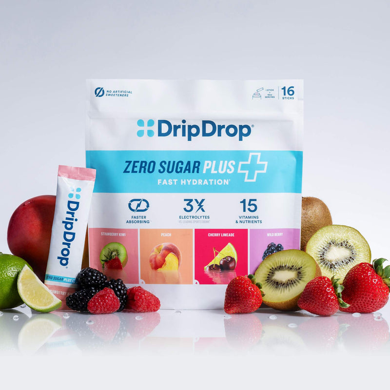 A stand-up pouch of DripDrop Zero Sugar Plus fast hydration powder, shown with a smaller single-serve stick pack in front. The package is white and light blue with colorful fruit flavor panels, surrounded by fresh strawberries, kiwi, blackberries, raspberries, a lime, and a red apple on a clean white studio background.