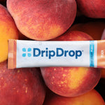 A DripDrop Zero Sugar Plus Peach flavor stick pack placed horizontally across a pile of fresh peaches.