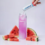 A hand pours DripDrop powder from a white and blue sachet into a clear bottle filled with pink liquid, surrounded by watermelon slices on a clean white background.