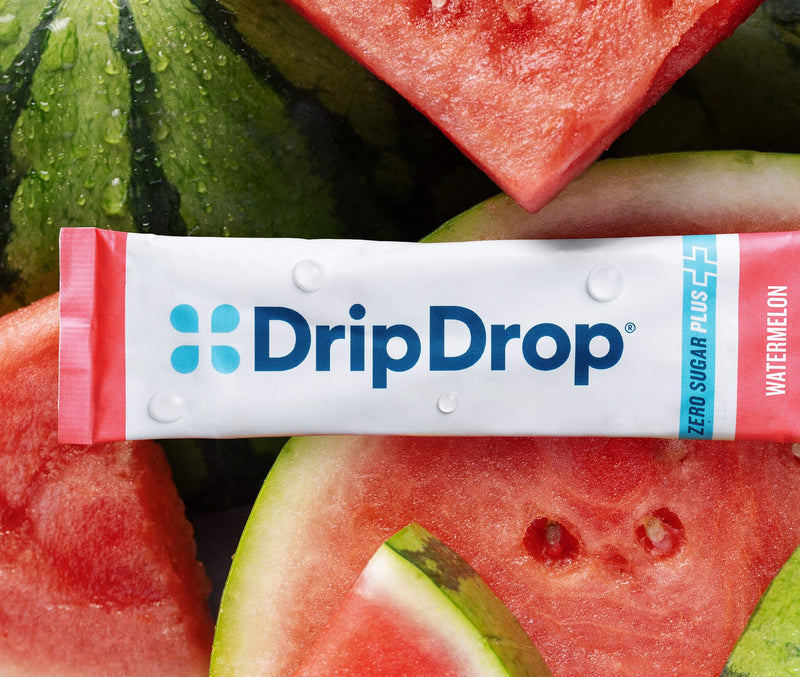 A DripDrop Zero Sugar Plus+ watermelon flavor stick pack, placed horizontally over a close-up background of fresh watermelon slices.