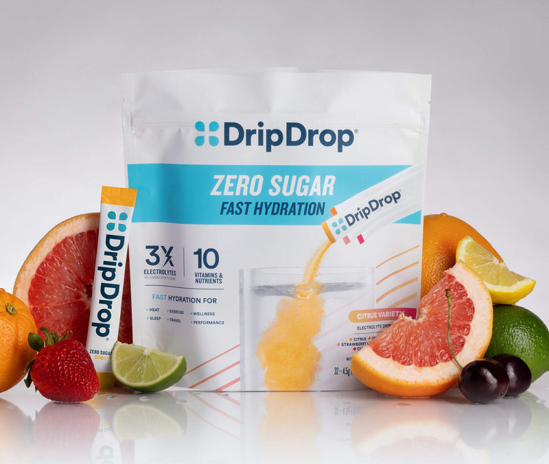 A stand-up pouch of DripDrop Zero Sugar Fast Hydration powder with a single stick pack beside it, surrounded by sliced citrus, grapes, and berries on a clean white studio background.