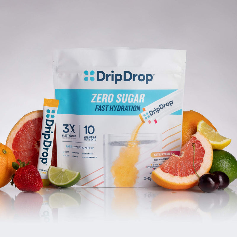 A stand-up pouch of DripDrop Zero Sugar Fast Hydration powder with a single stick pack beside it, surrounded by sliced citrus, grapes, and berries on a clean white studio background.
