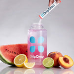 A clear plastic bottle with a pink drink inside and blue DripDrop logo graphics, with a hand pouring a DripDrop powder stick into the bottle. Watermelon, lemon, lime, and peach slices are arranged around the bottle on a light gray background.