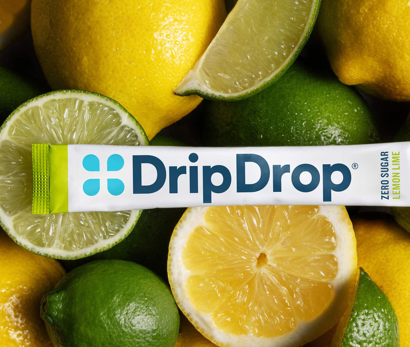 A DripDrop lemon lime zero sugar stick pack laid horizontally across a close-up arrangement of whole and sliced lemons and limes.