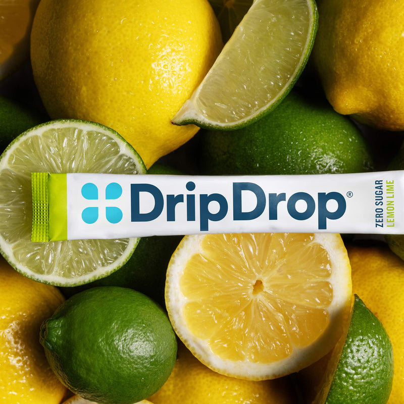 A DripDrop lemon lime zero sugar stick pack laid horizontally across a close-up arrangement of whole and sliced lemons and limes.