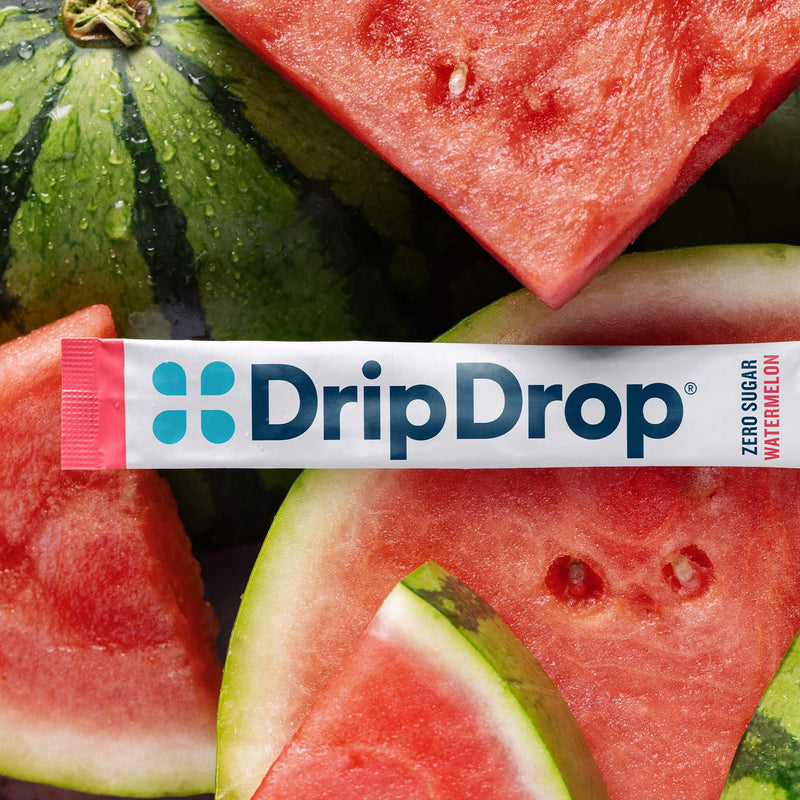 A DripDrop watermelon flavor zero sugar stick pack laid horizontally across a close-up background of sliced watermelon and a whole watermelon.