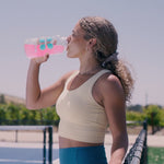 Girl drinking a pink liquid from a water bottle on a tennis court