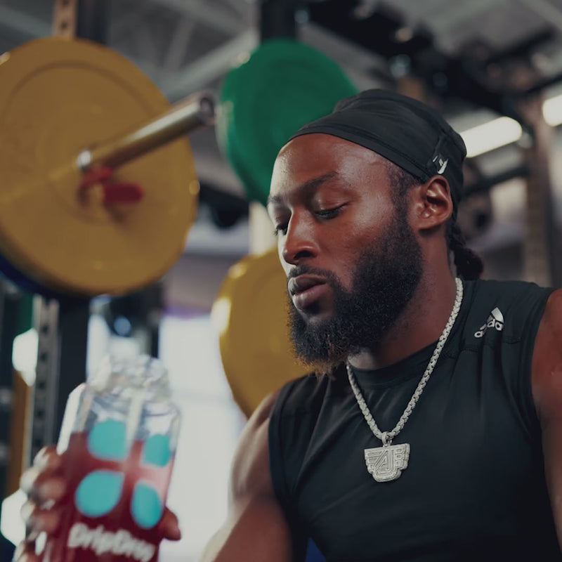 Man drinking red liquid from a water bottle in a gym setting