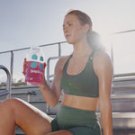 Woman on a set of bleachers drinking pink liquid out of a water bottle