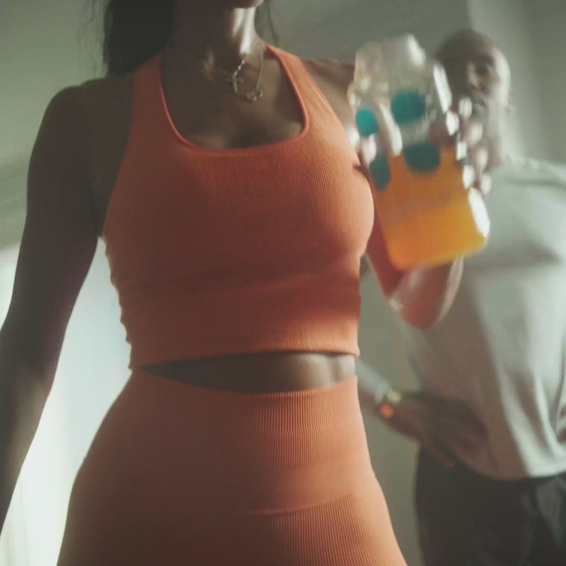 Woman in an orange workout set drinking orange liquid from a water bottle