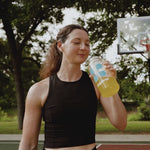Woman on a basketball court drinking orange liquid out of a water bottle