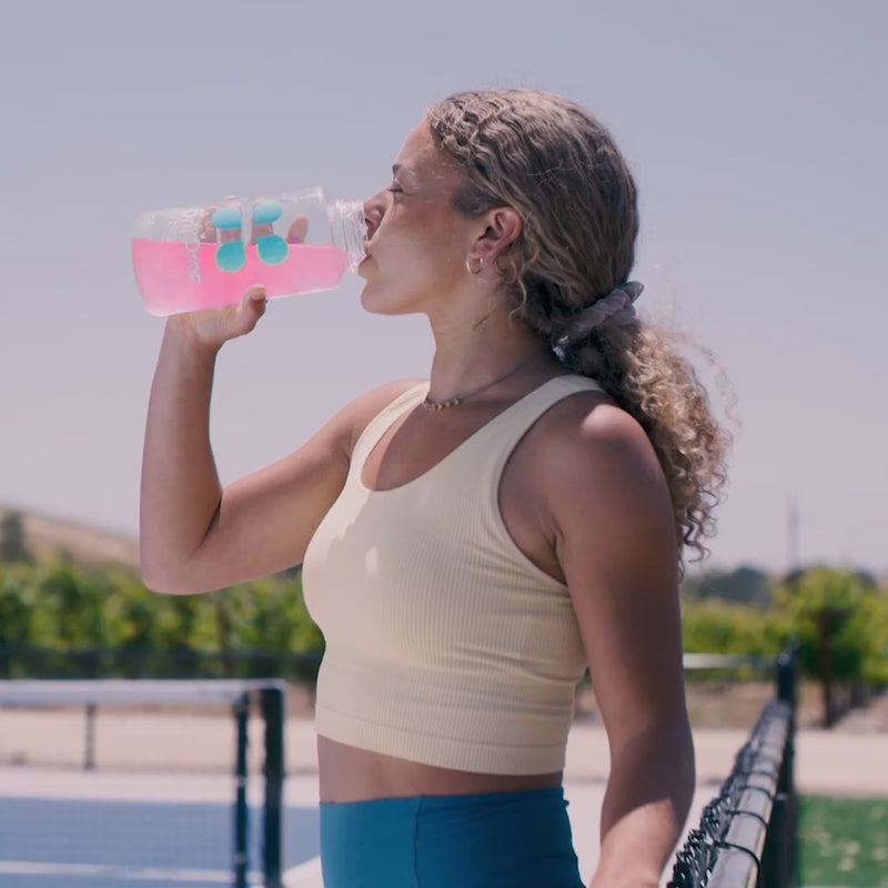 Woman drinking pink liquid from a water bottle on a tennis court